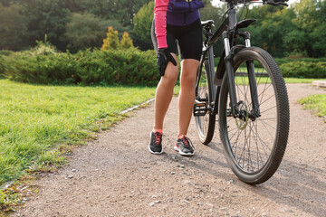Fototapeta na wymiar Woman with injured knee and bicycle outdoors, closeup. Space for text