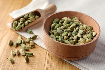Bowl and scoop of dry cardamom pods on wooden table