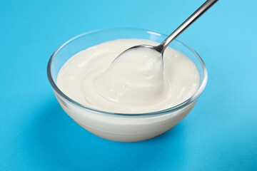 Eating tasty organic yogurt from bowl on light blue background
