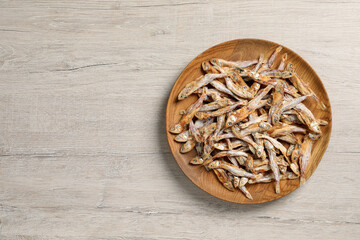 Obraz na płótnie Canvas Plate of tasty dried anchovies on light wooden table, top view. Space for text