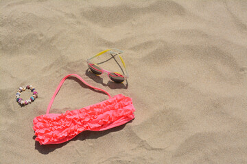 Sunglasses, bra and bracelet on sand, above view with space for text. Beach accessories
