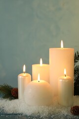 Burning candles with fir tree branch, cones and artificial snow on blue wooden table. Christmas atmosphere