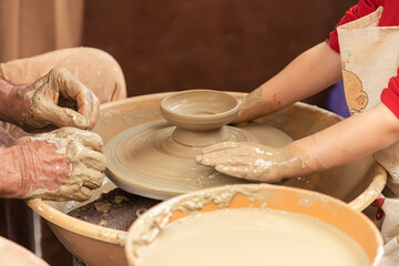 hands of a potter and a girl while the potter teaches the girl to model a clay cup