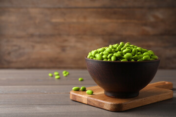 Bowl of delicious edamame beans on wooden table, space for text