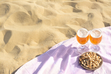 Fototapeta na wymiar Glasses of cold beer and pistachios on sandy beach, above view. Space for text