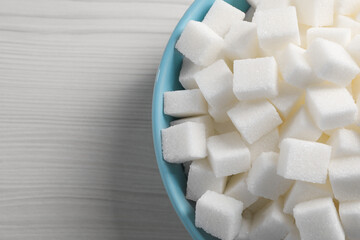 White sugar cubes in bowl on wooden table, top view. Space for text
