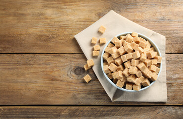 Brown sugar cubes on wooden table, flat lay. Space for text