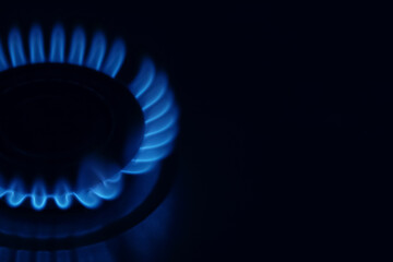 Gas cooktop with burning flame in darkness, closeup. Space for text