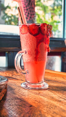 Glass of pink strawberry milkshake  served with crushed ice, fruits, with chocolate sauce and candy chips. Strawberry smoothie