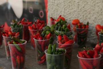 Many plastic cups with fresh chilli peppers on grey counter at market