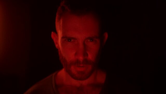 Angry man open eyes, awakes in hell, looking at camera with fury, rage, his face lit with fire flames, grief, sorrow. Male starring at enemy on war with aggresive emotions and insane devilish look.