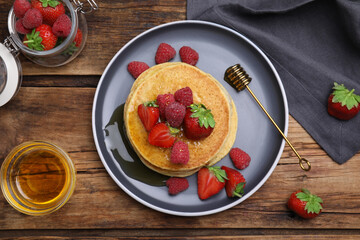 Tasty pancakes served with fresh berries and honey on wooden table, flat lay