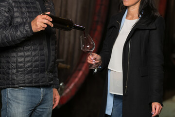 Cellar master, or winemaker pouring red wine for a woman to taste it and explaining wine varietals to her