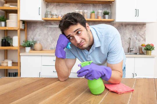 Tired and bored man cleaning table in the kitchen after cleaning house. Exhausted household concept	
