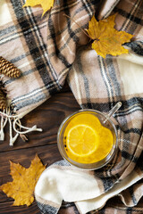 Fototapeta na wymiar Seasonal autumn concept with drink. Cup of hot sea ​​​​buckthorn tea with lemon, warm scarf and maple leaves on rustic background, creative flat lay. View from above.