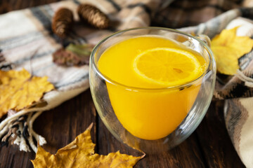 Seasonal autumn concept with drink. Cup of hot sea ​​​​buckthorn tea with lemon, warm scarf and maple leaves on rustic background.