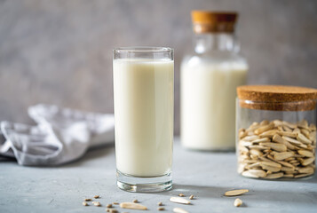 Sunflower milk in a glass and bottle, raw seeds in jar, napkin on concrete background.