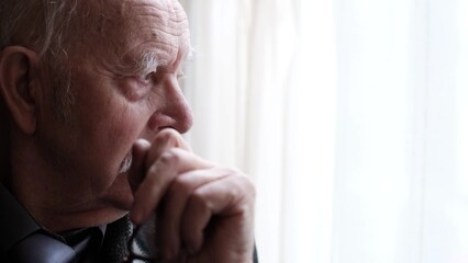 Portrait of upset grandfather by the window, close up portrait of an elderly man who is depressed
