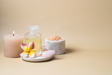 Natural massage oil, frangipani flower and sea salt scrab on beige background for wellness centre or spa cocnept.