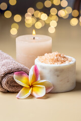 Beauty spa salon and wellness centre concept .Burning candles, sea salt scrub , frangipani flower and towel on beige background with bokeh.Copy space