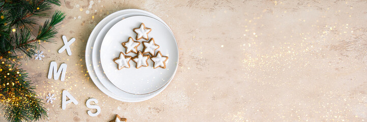 Christmas treat banner. Star shape ginger cookies with sugar icing on white plate with XMAS letters and fur branch.