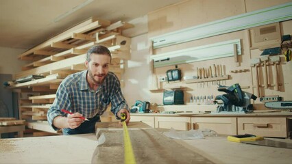 Attractive Carpenter Using a Tape Measure Ruler to Measuring Wood Board in a Loft Studio with Tools on the Walls. Woodworking. Manual Labor. Factory. Carpentry, Craftsmanship, and Handwork Concept.