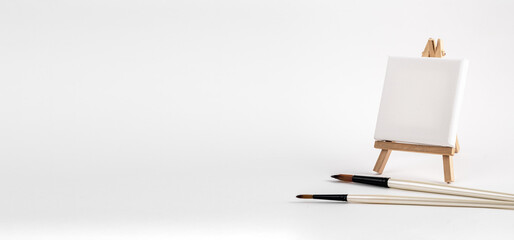Mini easel with white blank canvas, paintbrushes. Art banner, creative studio ads background