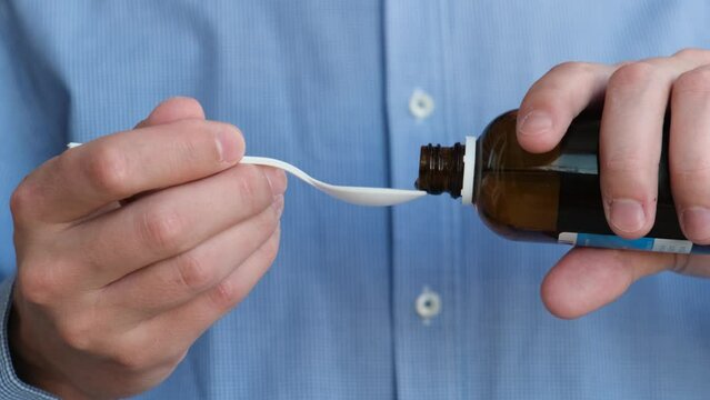 A man pours cough syrup or other medicine into a serving spoon, close-up