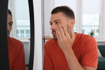 Sleep deprived man looking at himself in mirror indoors