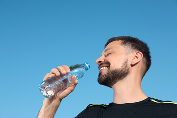 Happy man drinking water against blue sky on hot summer day. Refreshing drink