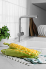 Tasty sweet corn cobs on white countertop in kitchen