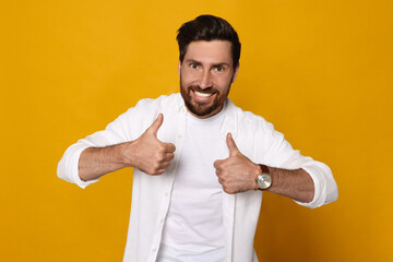 Handsome bearded man showing thumbs up on orange background