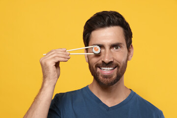 Happy man hiding his eye with tasty sushi roll on orange background © New Africa