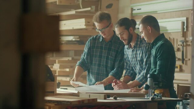 Carpenters Working in a Loft Studio on a New Product Design are Looking at a Blueprint Project and Having a Conversation. Woodworking. Manual Labor. Carpentry, Craftsmanship, and Handwork Concept.