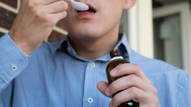 A man drinks a portion of liquid cough syrup from a spoon, close-up