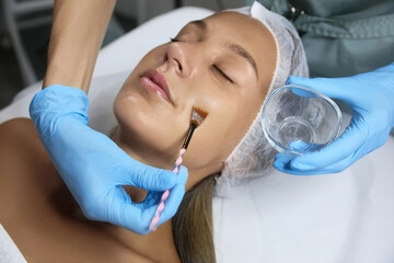 Naklejka premium Cosmetologist applying chemical peel product on client's face in salon