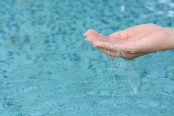 Water pouring into girl's hand above pool, closeup. Space for text