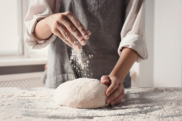 Woman sprinkling flour over dough at table in kitchen, closeup