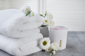 Scented candle, folded towels and eustoma flowers on gray marble table