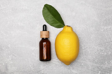 Bottle of essential oil with lemon and leaf on grey table, flat lay