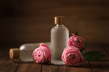 Bottles of essential rose oil and flowers on wooden table