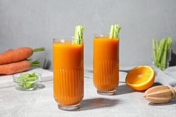 Glasses of tasty carrot juice with celery sticks on light grey table