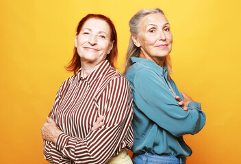 Two pretty elderly ladies stand next to each other with their arms crossed over their chests,...