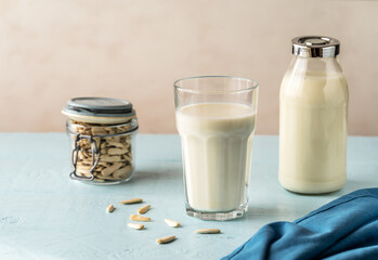 Sunflower milk in a glass and bottle, raw seeds in jar on light blue background with napkin.