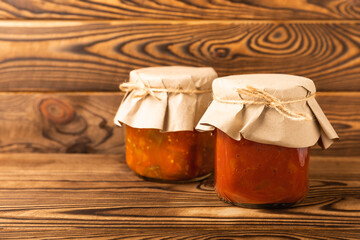 Glass jar of delicious canned lecho on a brown wooden background. side view. Salad in a jar.