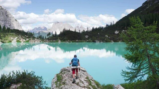 Young backpacker with backpack walking up the cliff to enjoy turquoise Lago di Sorapiss 1,925m altitude (mountain lake) view as he walking in Dolomite Mountains, Italy. Active people in nature concept
