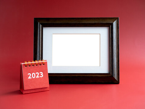 Template for photo frame for card with small red desk calendar with 2023 year number on red background, minimalist. Empty white blank space in vintage wooden picture frame.