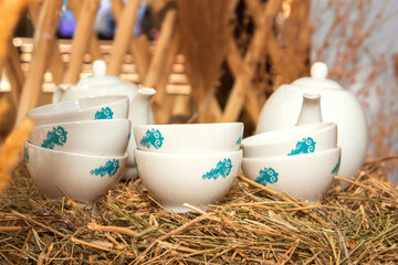 Porcelain teapot and cups with oriental ornaments stand on bales of hay against the background of the wall of the nomads' dwelling - the yurt.