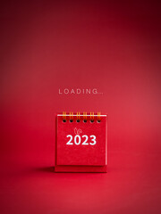 Loading to Merry christmas and happy new year 2023 background. Loading, text appears on small red desk calendar with 2023 year numbers on red background, minimalist, vertical style. - obrazy, fototapety, plakaty