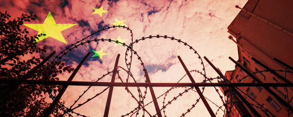 Barbed wire on iron fence of Chinese jail or border facility against China flag background